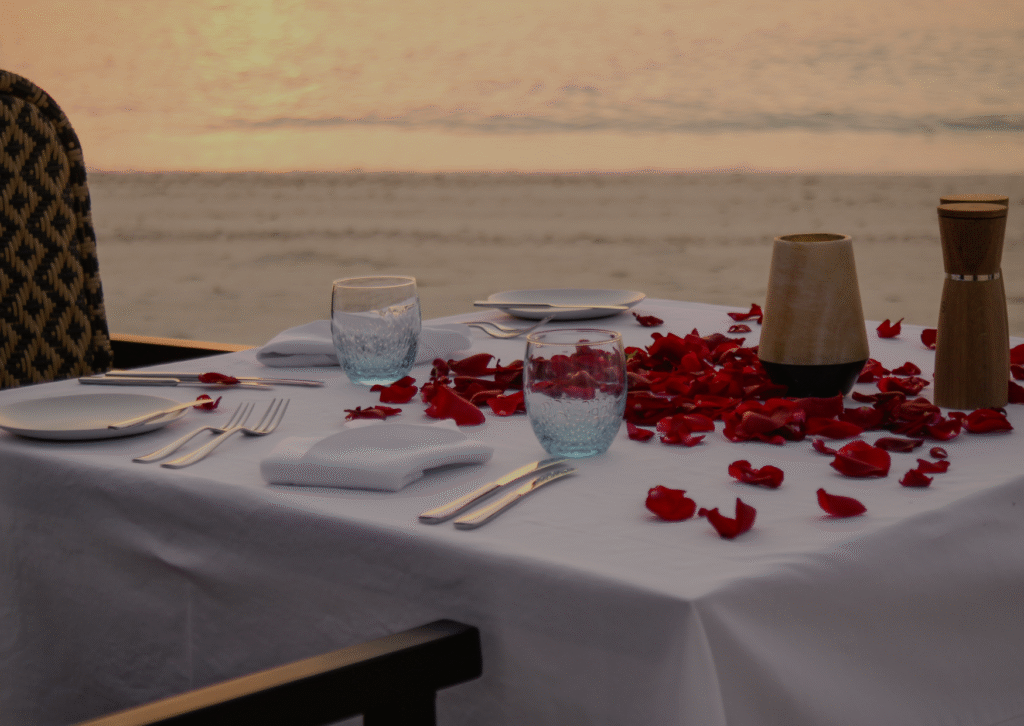 Current image: a table with glasses and petals on the seashore on the beach