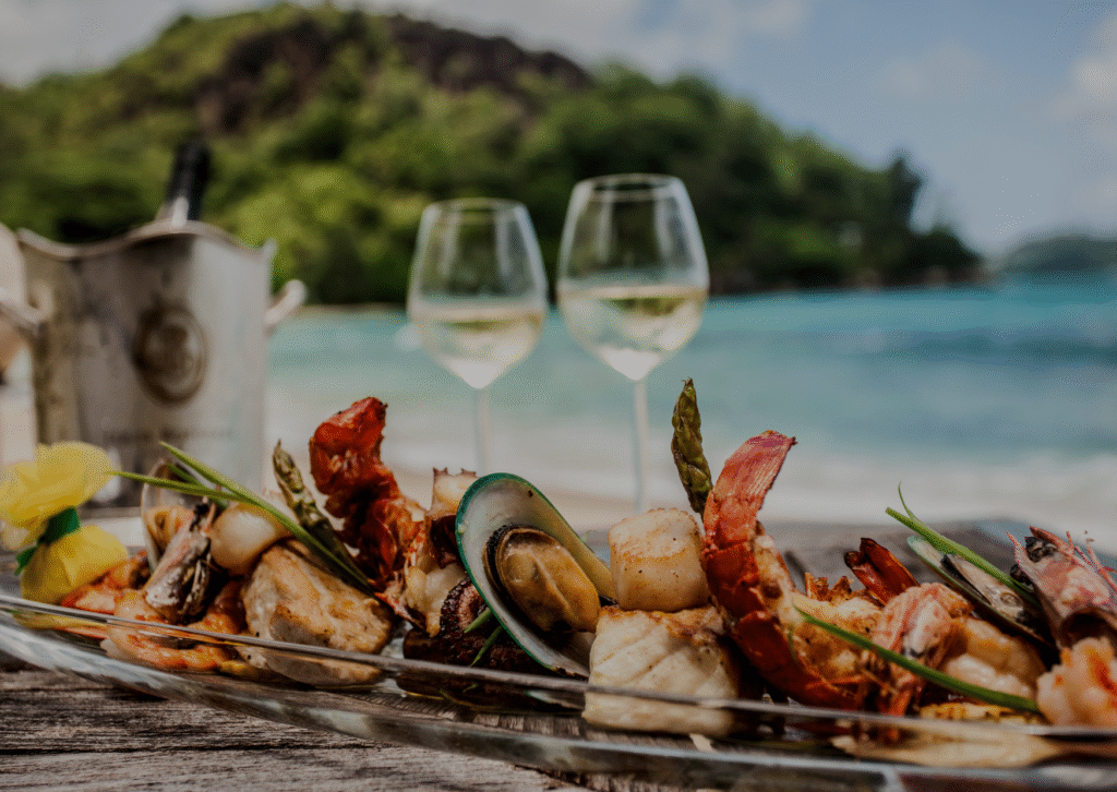 Current image: two glasses of wine with seafood in front of a beach